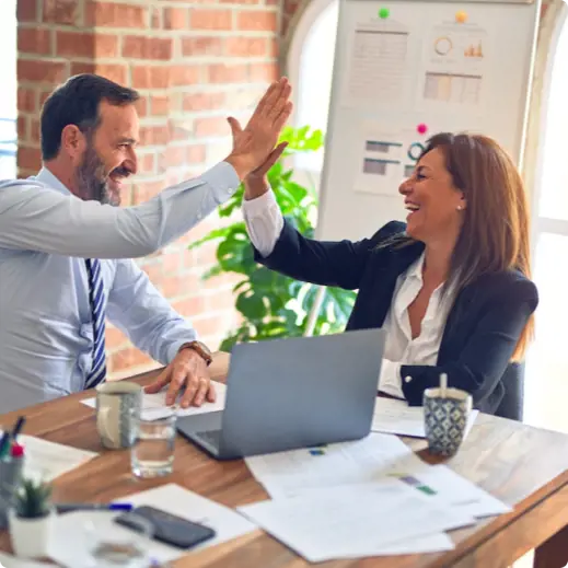 smiling man and woman in business attire high five over desk