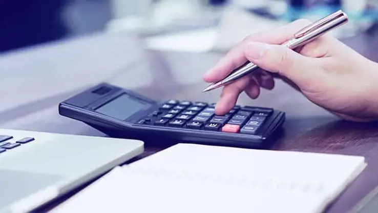 Side view of hand holding a pen with finger pressed on calculator