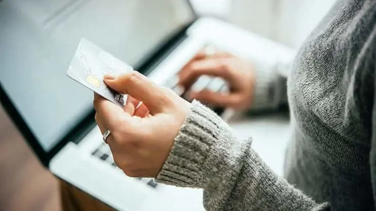 Aerial view of female hand holding a credit card in one hand and typing on a keyboard with the other hand