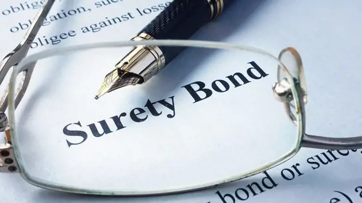 The words surety bond printed on paper with a pair of reading glasses and pen placed around it